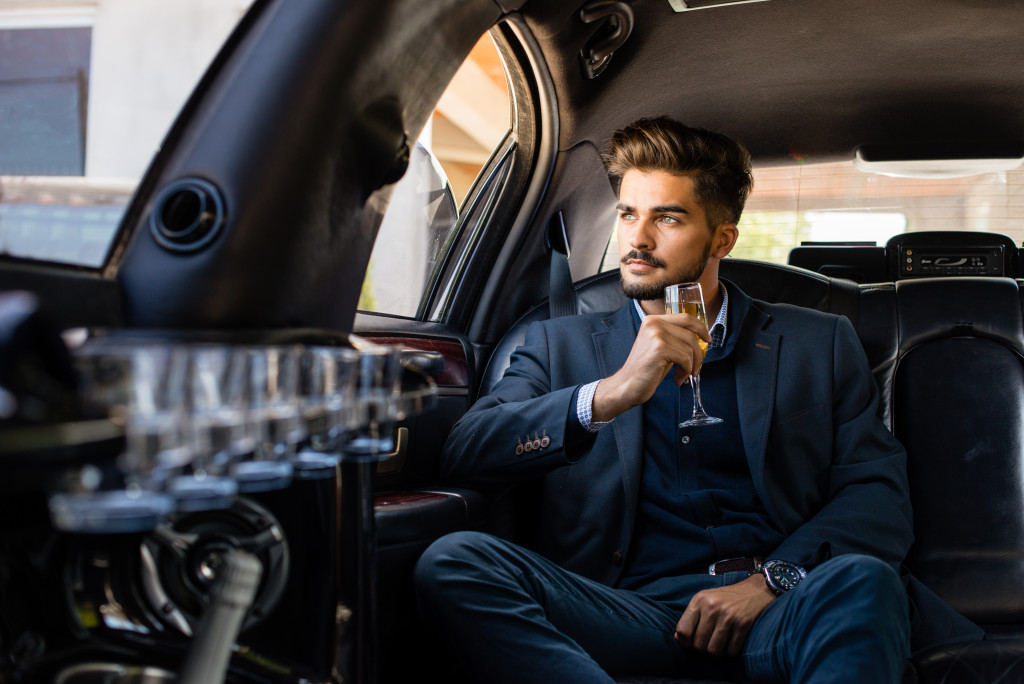 A man sits at the back of a car drinking